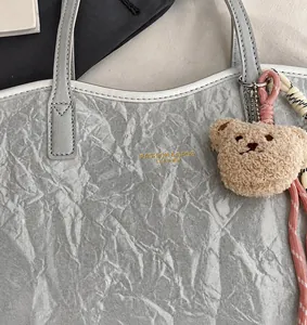 Detail of light gray textured leather tote bag with gold logo and plush bear charm