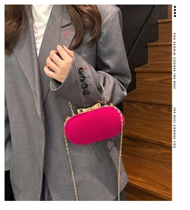 Model wearing a rose red velvet oval evening bag with a gold bow clasp and chain strap