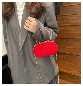Detailed view of red velvet clutch bag with golden bow clasp and chain strap held by model