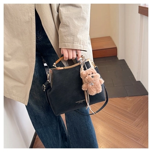 Détail du sac à main rétro avec poignée en bois et breloque ours en peluche sur trench-coat