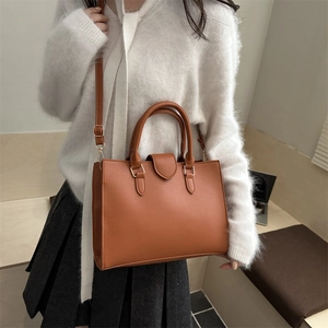 Brown faux leather tote bag with top handle and gold hardware shown on a model