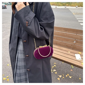 Detail view of a purple velvet oval evening bag with a golden bow clasp and chain strap