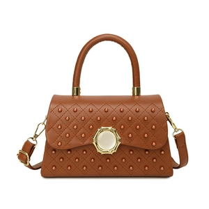 Sac à main matelassé marron avec clous et fermoir doré sur fond blanc pur et minimaliste