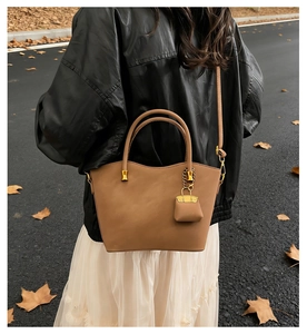 Detail of camel leather tote bag with mini bag charm shown on model in outdoor street style