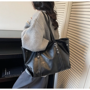 Detail of contrast white stitching and silver rivets on a black leather tote bag