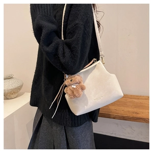 Modèle portant un sac coquille blanc cassé avec détail de charme d'ours en peluche