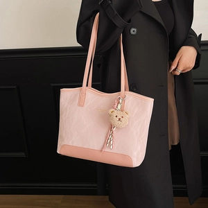 Pink pleated tote bag with bear charm and long straps worn over a black trench coat