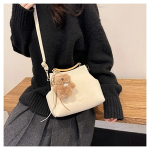 Détail du sac coquille blanc crème avec poignée dorée et accessoire charme d'ours en peluche