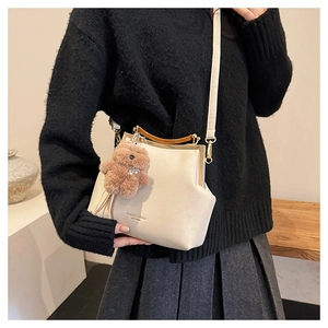 Détail du sac beige avec poignée en bois, fermoir métallique et breloque ours en peluche
