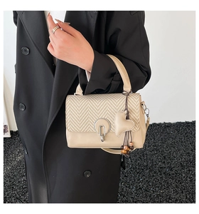 Detalle del bolso beige con solapa tejida, cierre metálico y colgante de corazón