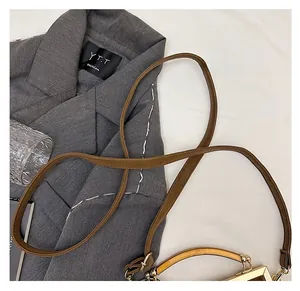 Détail d'une bandoulière en cuir marron avec crochets dorés et une poignée en bois