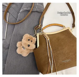 Détail du sac rétro marron avec poignée ambre et breloque ours en peluche sur un costume