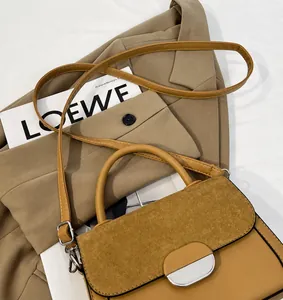Detail of camel patchwork saddle bag with suede texture and metal clasp on white background