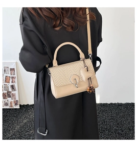 Detalle de bolso beige con colgante de corazón y textura tejida sobre una modelo