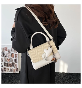 Detalle de bolso blanco con solapa tejida y colgante decorativo de corazón con madera