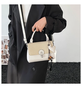 Detalle de bolso bicolor con solapa tejida, hebilla plateada y borla de corazón de perlas