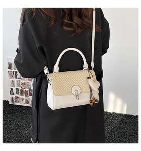 Detalle de un bolso bandolera chic con textura tejida y un colgante en forma de corazón