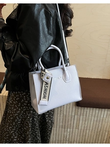 Detailed view of striped textured handbag with a wide fashion strap on a model shoulder