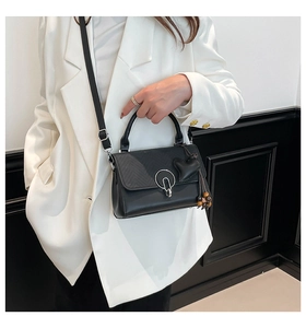 Detalle de bolso bandolera negro con hebilla plateada y colgante de corazón sobre blazer