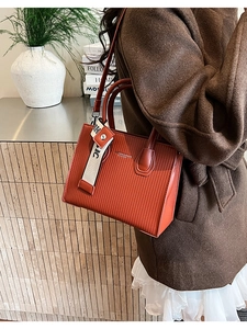 Close-up of structured orange-brown leather handbag with vertical stripes and fashion print