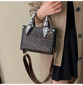 Close-up of leopard print handbag with silk scarf handle and wide fabric logo strap