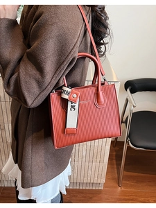 Close-up of caramel square bag with vertical pleated texture and striped webbing detail