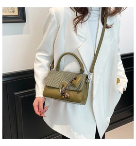 Detalle del bolso verde oliva con solapa de pata de gallo y colgante de corazón sobre blazer