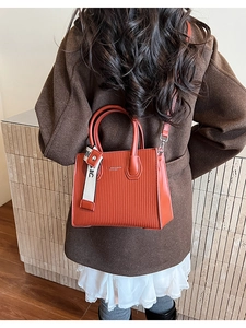 Close-up of brick red textured square handbag worn over a brown coat with strap detail