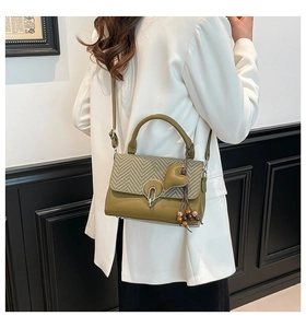 Detalle de bolso verde oliva con solapa tejida y amuleto de corazón llevado por modelo
