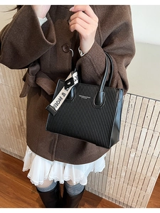 Detail of black pleated leather handbag with a patterned scarf and letter print
