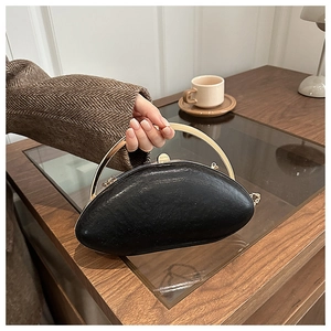 Detail of a black oval acrylic evening clutch featuring a golden top handle and metal chain