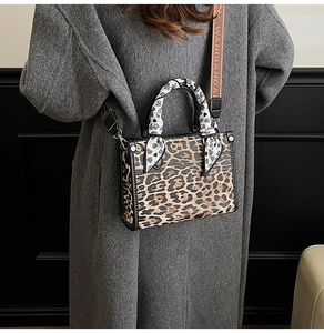 Detail of leopard print crossbody bag with heart scarf handle and wide branded strap