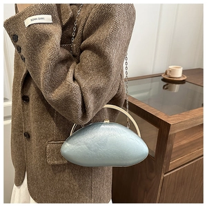 Detail of light blue oval acrylic clutch with golden ring handle and pearlescent finish
