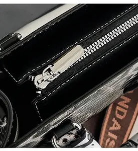 Close-up of silver metal zipper and decorative scarf on black polished leather handbag