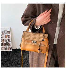 Detail of woven texture handbag with rotating metal clasp held by model in brown coat