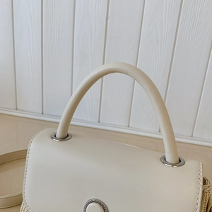 Close-up of cream white leather bag showing arc handle and silver metal ring hardware