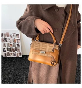 Detail of a brown plaid crossbody bag with a metal twist lock and heart-shaped charm