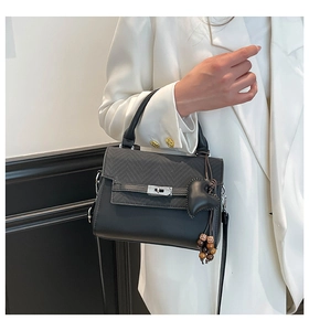 Detail of a black plaid satchel bag with silver clasp and heart-shaped charm on a model
