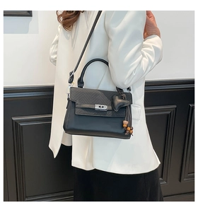 Detail of black top handle bag featuring herringbone texture and heart charm tassel