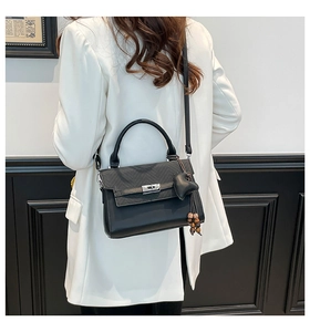 Detail view of a black leather handbag featuring a silver twist lock and heart tassel charm