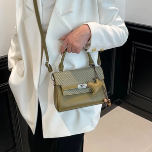 Olive green crossbody Kelly bag with woven chevron flap and heart charm on white suit