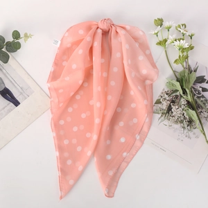 Pink polka dot chiffon scarf with knot design, styled with flowers on white background