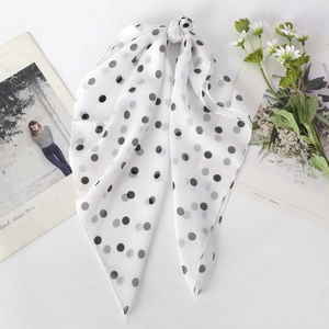 Detail of white chiffon scarf with black polka dots tied in a bow next to a daisy flower