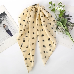 Detail of beige chiffon scarf with black polka dots and knot design on white background