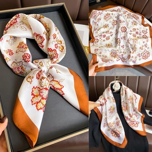 Détail d'un foulard en soie à fleurs avec base ivoire et bordure orange sur un pull