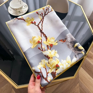 Detail of silk-like scarf with magnolia print and yellow rolled edges on a table
