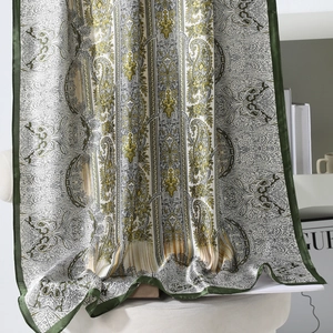 Luxurious green paisley silk scarf with vintage floral patterns draped on a white chair