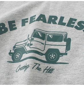 Close-up of grey jersey fabric with green vintage off-road car and Be Fearless print
