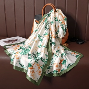 Bamboo leaf print silk scarf draped over a luxury handbag in a high-end setting