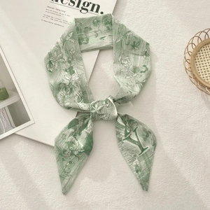 Detail of green floral skinny scarf tied in a bow on a textured linen background